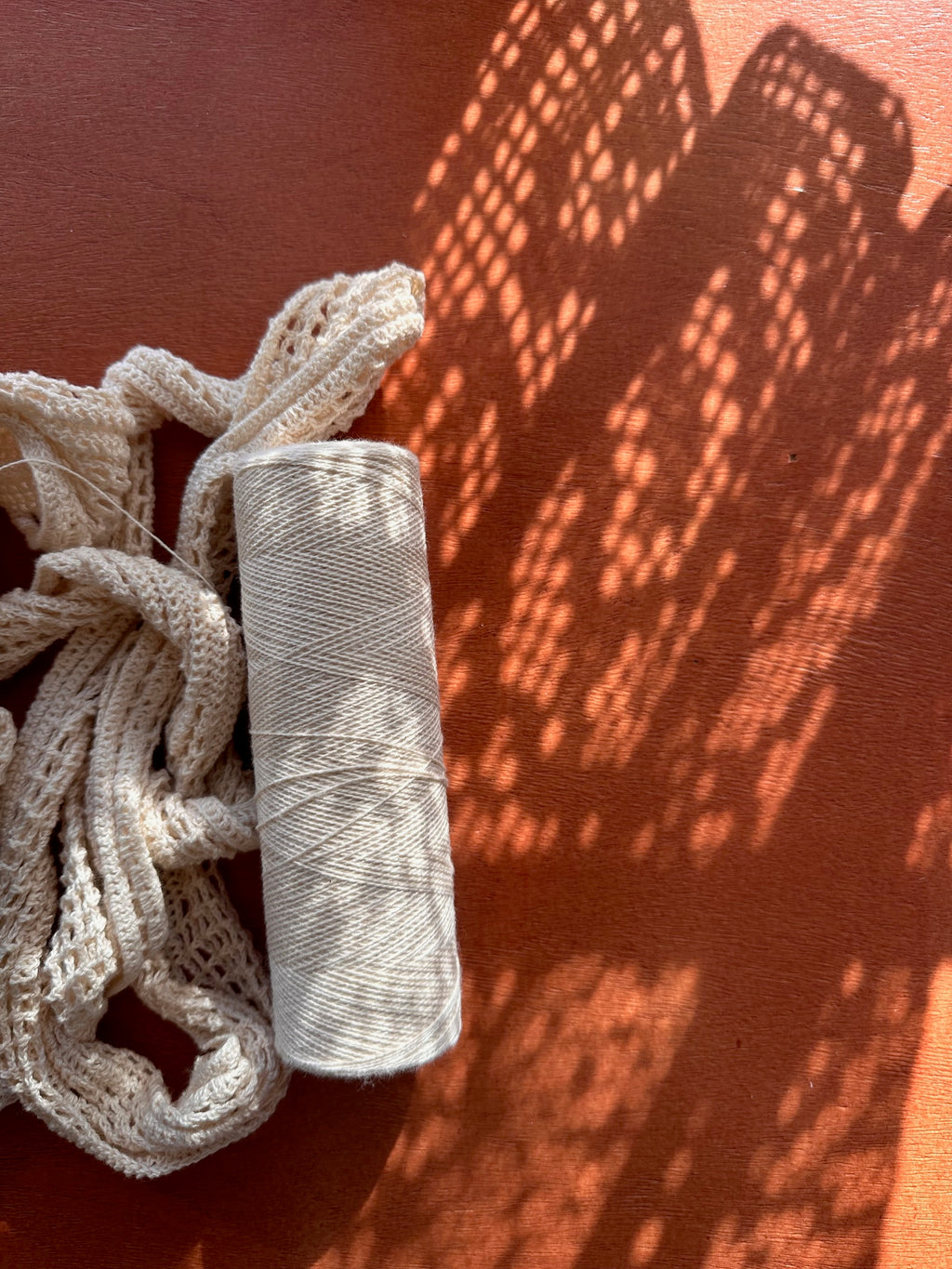 Spool of white thread on a wooden table with shadow patterns