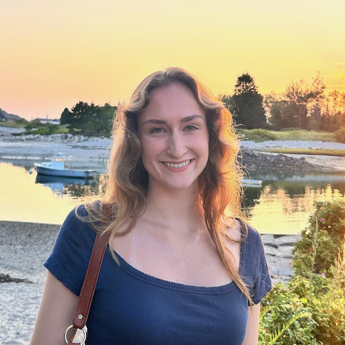 Woman with long blonde hair standing by an ocean inlet at sunset.