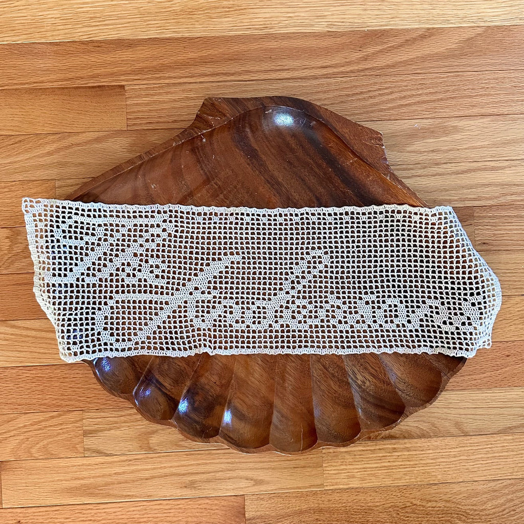 Wooden shell tray with a white lace doily on a wooden floor
