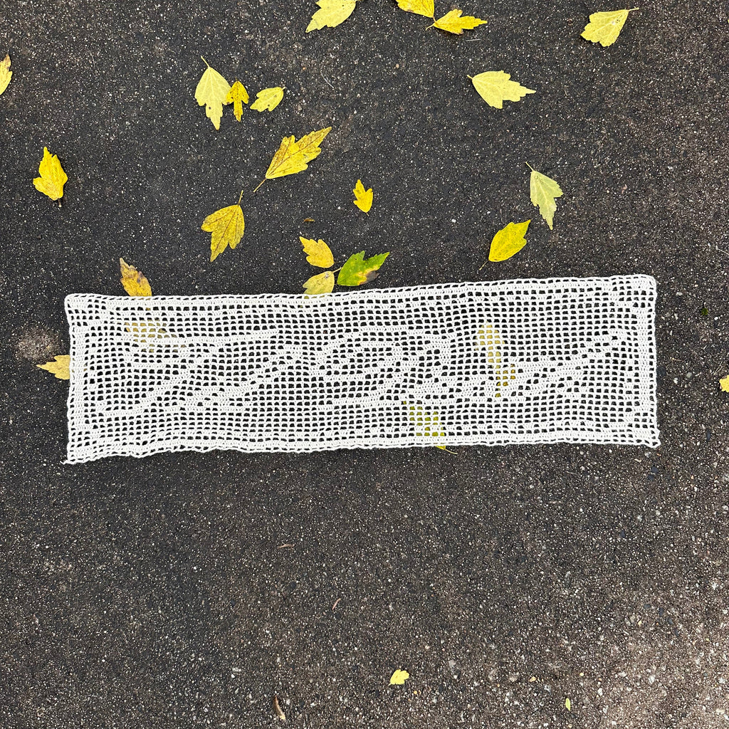 White lace filet crochet textile on dark pavement with scattered yellow leaves