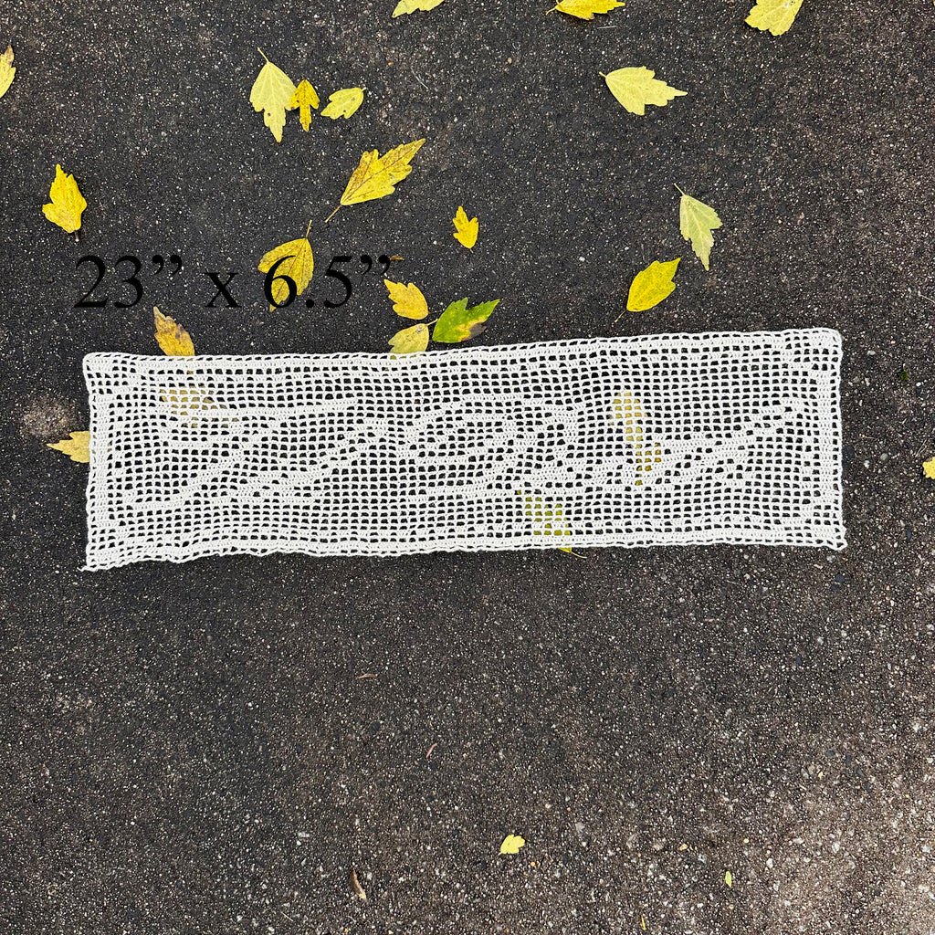 Rectangular white lace doily on dark pavement with scattered yellow leaves.